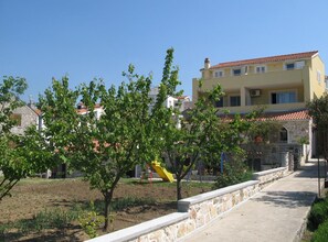 A residential area with a paved walkway, a playground with a slide, and buildings with red-tiled roofs. - One Bedroom Apartment with Balcony and Sea View-ŽUTI (Murter)