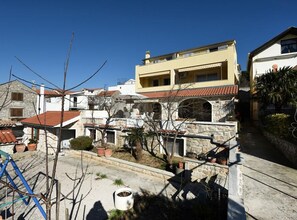 A residential area with stone buildings, a paved courtyard, and a clear blue sky. - Standard One Bedroom Apartment with Balcony and Sea View-CRVENI (Murter)