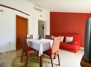 A dining area with a table set for two, a red sofa, and a television. - Standard One Bedroom Apartment with Balcony and Sea View-CRVENI (Murter)