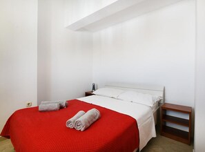 Ein Einzelzimmer mit rotem Bettbezug, weißen Kissen und einem Nachttisch aus Holz.