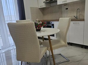 Una cocina moderna con una mesa de comedor redonda, dos sillas, un jarrón con flores y un horno empotrado.