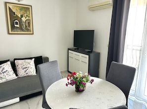 A modern living room with a sofa, a television, a cabinet, and a round table with a flower vase. - One Bedroom Apartment with Balcony and City View 2 (Trogir)