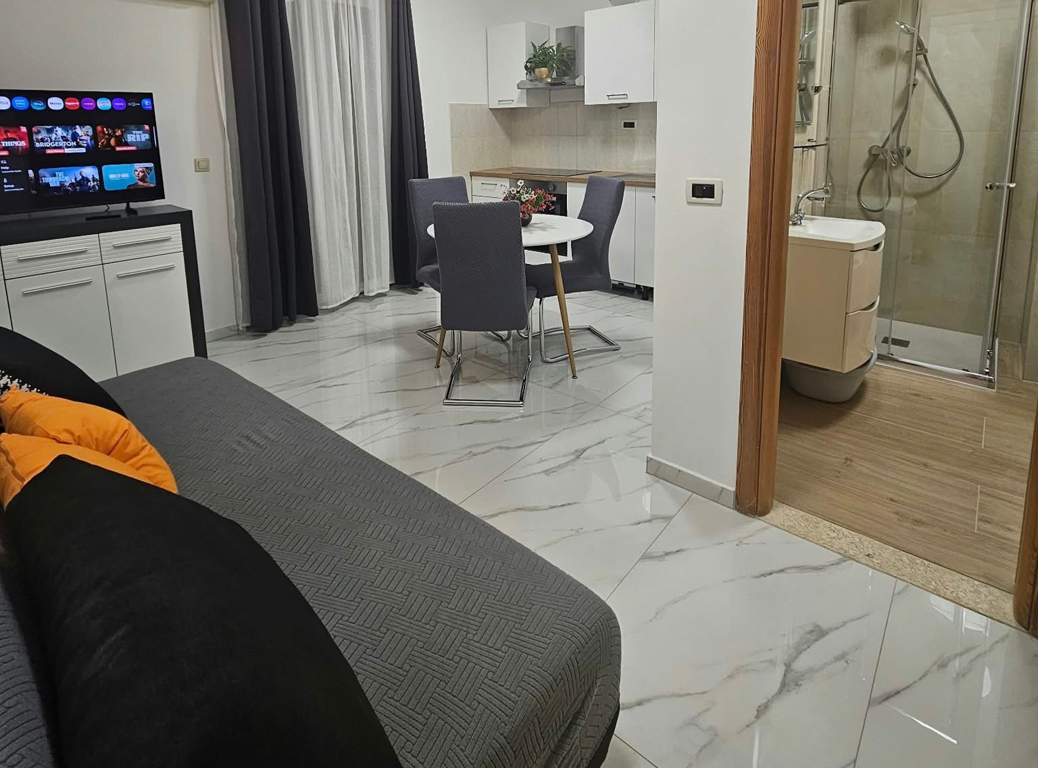 Ein modernes Wohnzimmer mit einer Couch, einem Essbereich mit Tisch und Stühlen, einer Küche mit Schränken sowie einem Duschbereich.