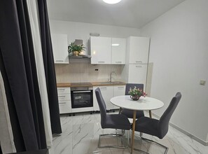 A compact kitchen with white cabinets, a built-in oven, and a dining area with a round table and two chairs. - One Bedroom Apartment with Pool 2 (Trogir)