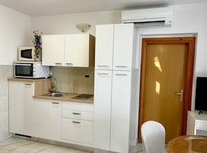 Cozinha compacta com armários brancos, micro-ondas, torradeira, pia e ar condicionado.