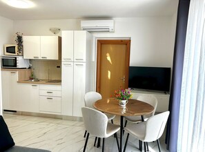 A modern kitchen with white cabinets, a microwave, and a dining area with a wooden table and four chairs. - Two Bedroom Apartment with Balcony and Garden View (Trogir)