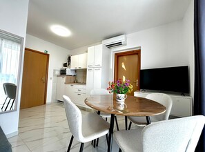 A compact living space with a dining area, kitchenette, and a television. - Two Bedroom Apartment with Balcony and Garden View (Trogir)