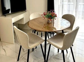 A modern dining area with a round table, four chairs, a vase of flowers, and a television on a cabinet. - Two Bedroom Apartment with Balcony and Garden View (Trogir)