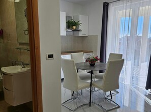 A modern kitchen with white cabinets, a built-in oven, and a dining area with a round table and four chairs. - One Bedroom Apartment with Balcony (Trogir)