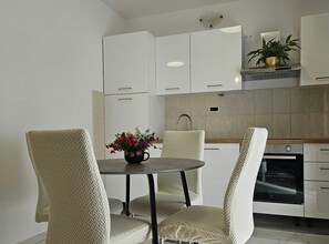 Ett modernt kök med vita köksluckor, ett runt matbord och två stolar med ett vävt mönster.