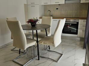 A modern kitchen with a dining area, featuring a round table with chairs, a built-in oven, and a tiled backsplash. - One Bedroom Apartment with Balcony (Trogir)