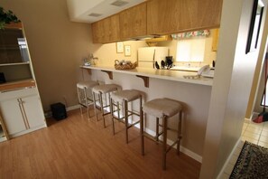 A kitchen with wooden cabinets, a white countertop, and three bar stools. - Grab a glass of wine and enjoy the Lake Views! (Palm Desert)