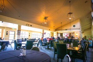 Un comedor amplio con varias mesas y sillas, una zona de bar y un techo alto con lámparas colgantes.