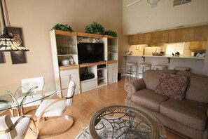 A living room with a glass coffee table, a beige sofa, and a TV on a stand. - Grab a glass of wine and enjoy the Lake Views! (Palm Desert)
