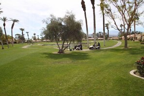 A golf course with a clear path, palm trees, and a building in the background. - Grab a glass of wine and enjoy the Lake Views! (Palm Desert)