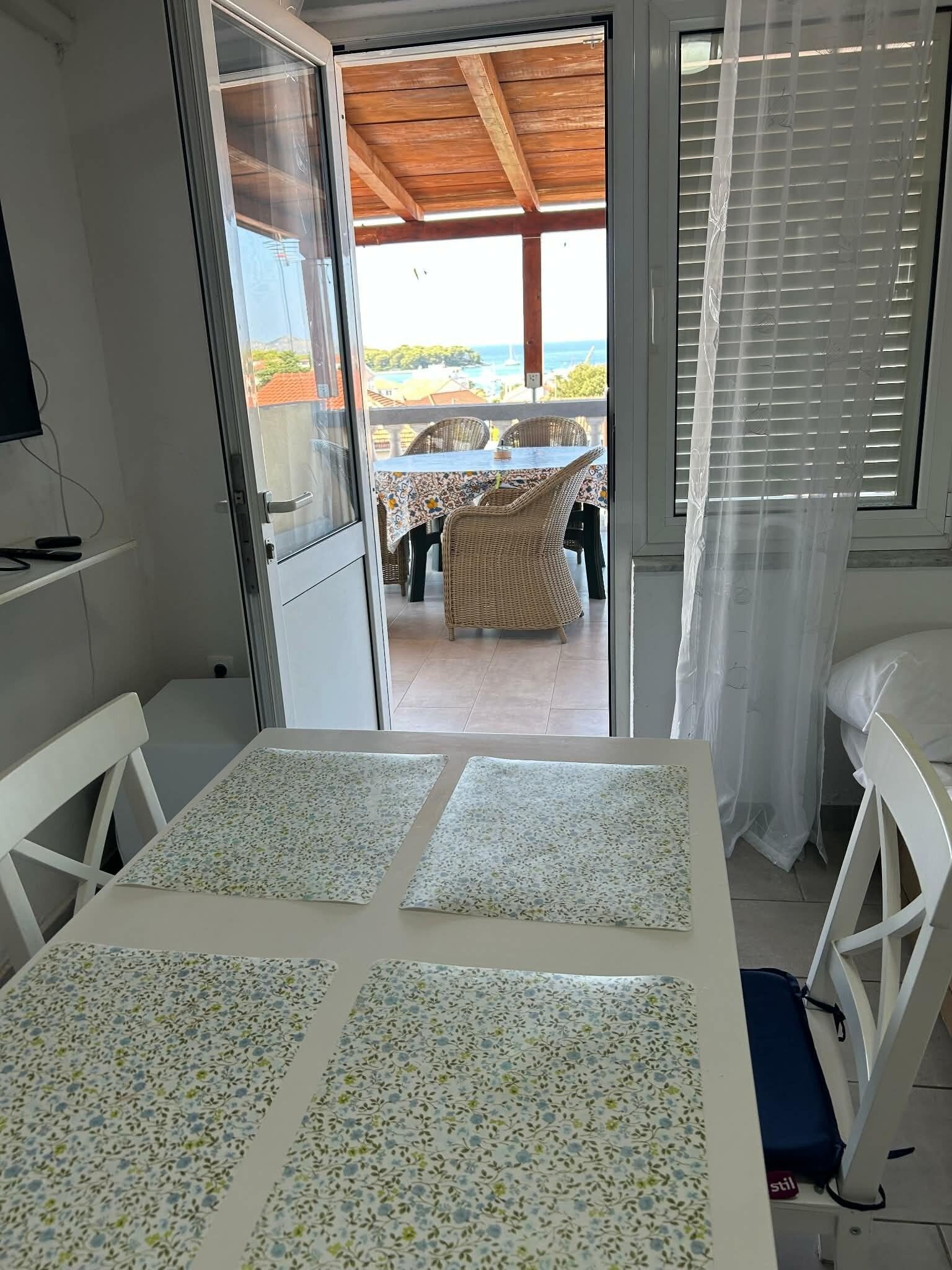 A room with a table and chairs, a view of the sea, and a covered outdoor area.