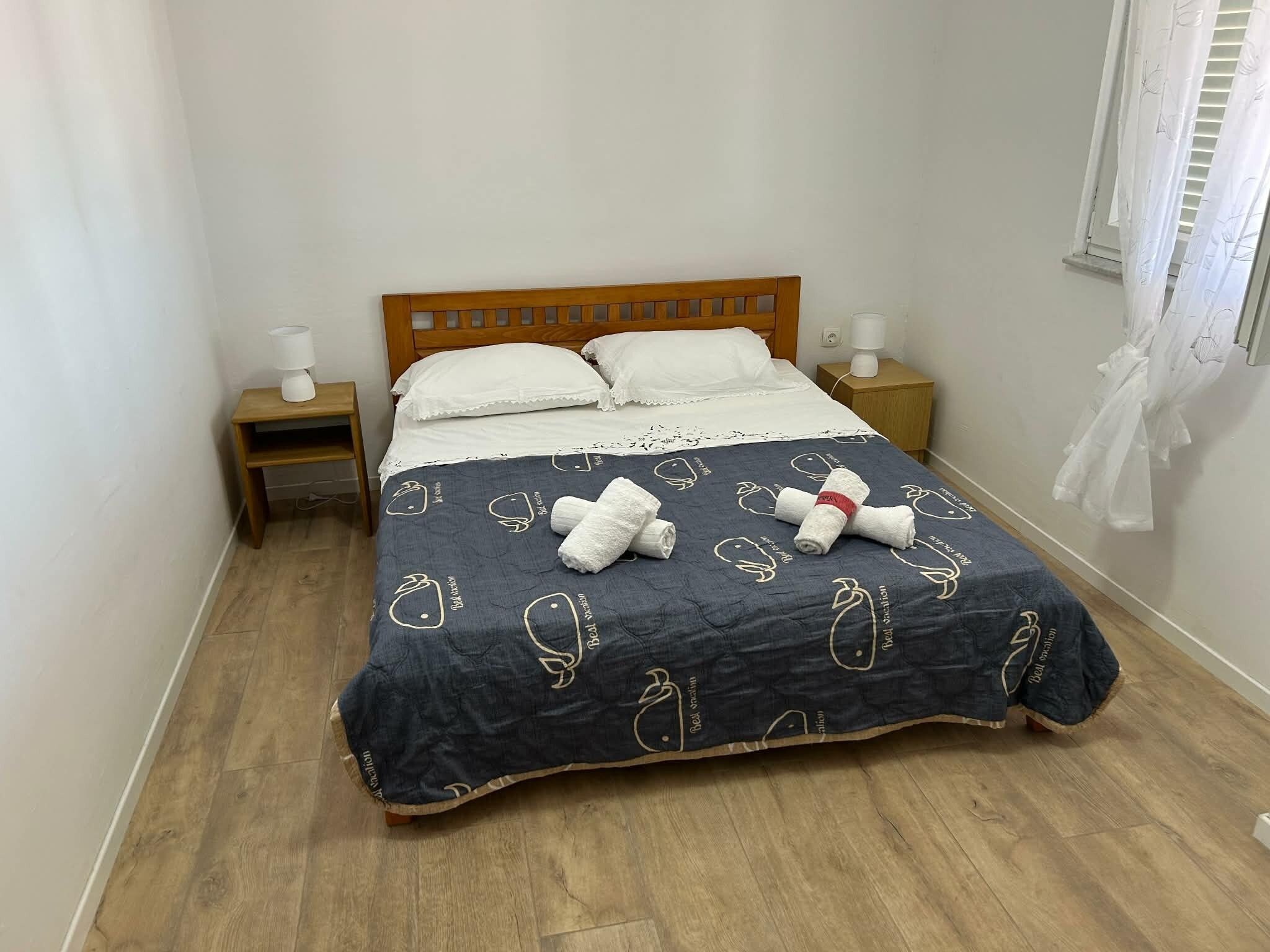 A bed with a dark blue blanket featuring white patterns, two white pillows, and two bedside lamps on wooden nightstands.