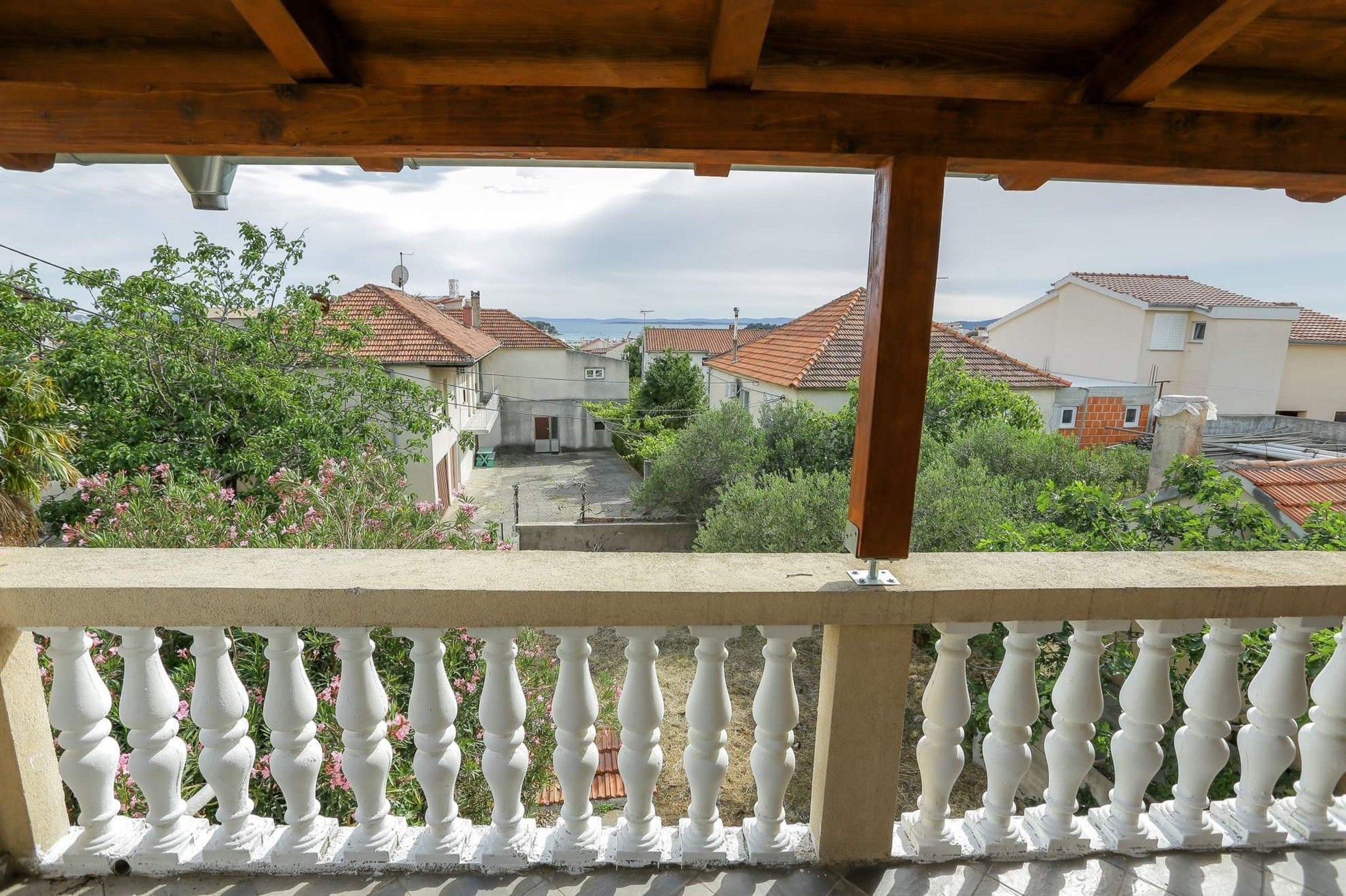 A balcony with a white balustrade overlooking a residential area with terracotta roofs.