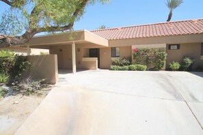 A building with a covered parking area, a red-tiled roof, and a small garden with various plants. - Great Views and Palm Desert Flare! (Palm Desert)