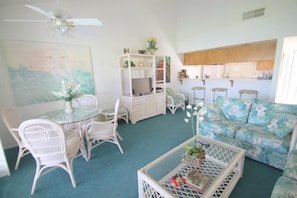 A living room with a dining table, chairs, a sofa, a ceiling fan, and a kitchen area in the background. - Great Views and Palm Desert Flare! (Palm Desert)