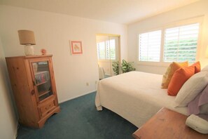 A bedroom with a bed, a wooden cabinet, a window with blinds, and a small table. - Great Views and Palm Desert Flare! (Palm Desert)