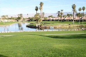A golf course with a pond, palm trees, and a clear sky. - Great Views and Palm Desert Flare! (Palm Desert)
