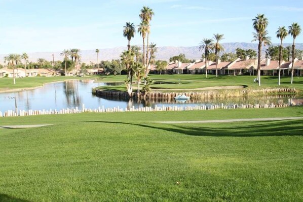 A golf course with a pond, palm trees, and a clear sky. - Great Views and Palm Desert Flare! (Palm Desert)