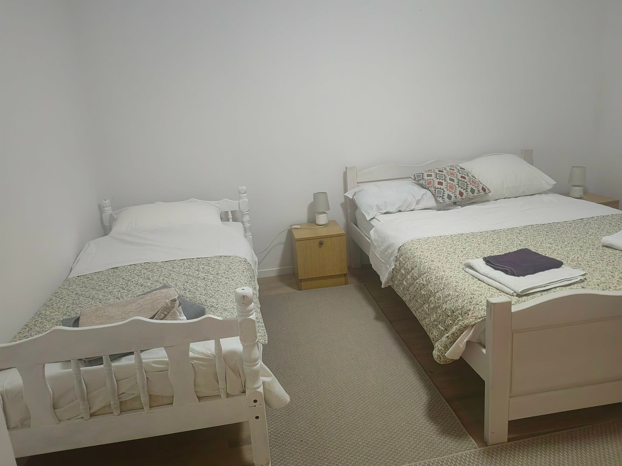 Habitación con dos camas individuales, cada una con mesita de noche, lámpara y almohada estampada. La habitación tiene una distribución sencilla, con paredes lisas y suelo cubierto de alfombra.