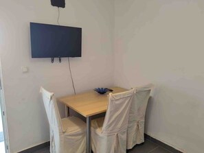 A room with a wooden table, four chairs, a flat-screen TV mounted on the wall, and a power outlet on the wall. - Apartment 'Mediterranean' with Sea View, Wi-Fi and Air Conditioning (Pakoštane)