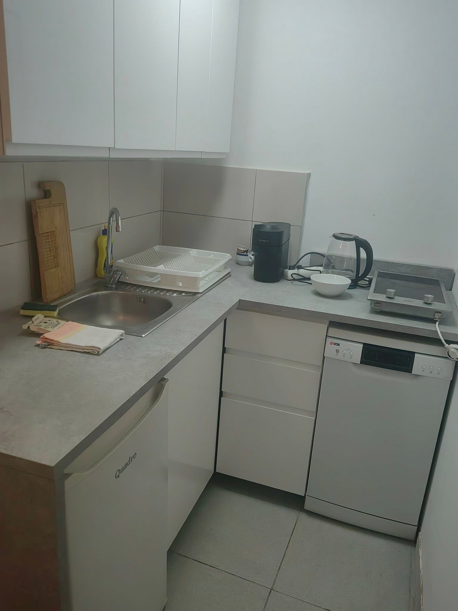 Una cocina compacta equipada con lavavajillas, hervidor de agua, cafetera y tabla de cortar.