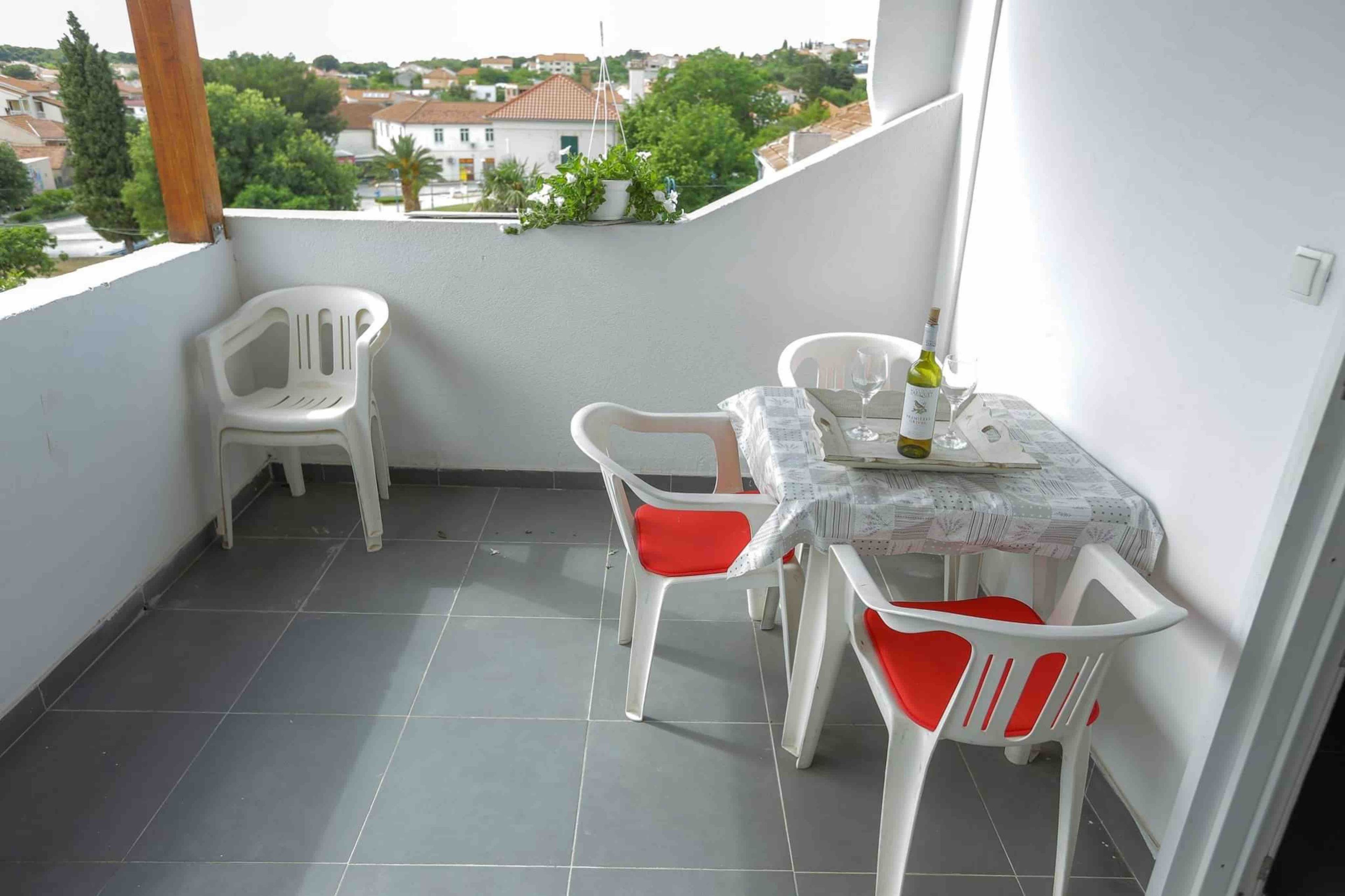 Uma varanda com mesa e cadeiras, uma garrafa de vinho e vista do bairro.