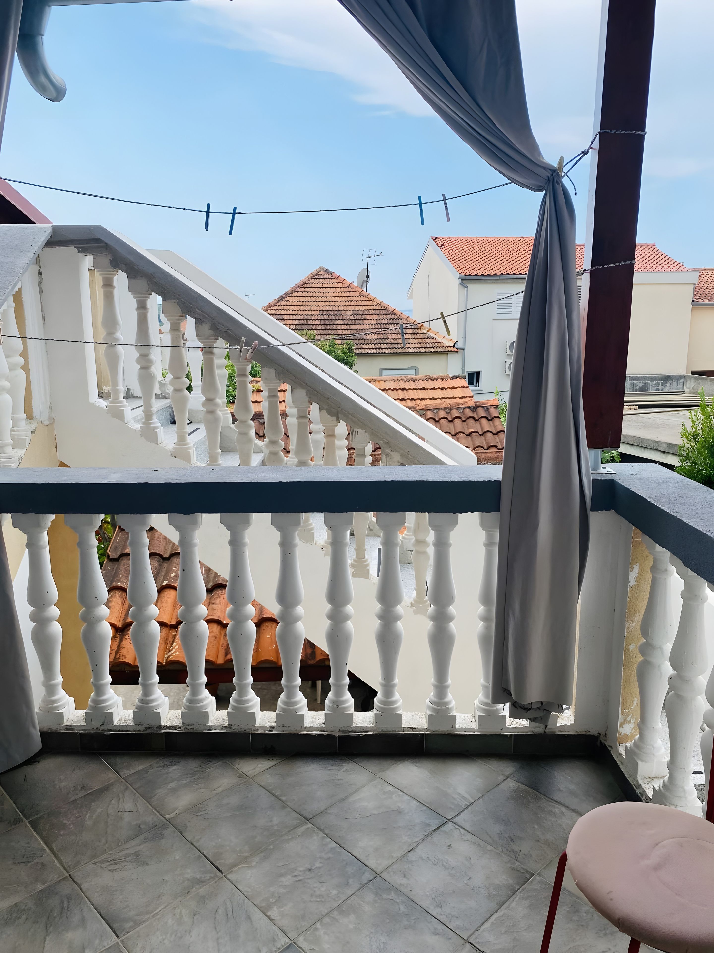 A balcony with white balustrades, a grey curtain, and a tiled floor.