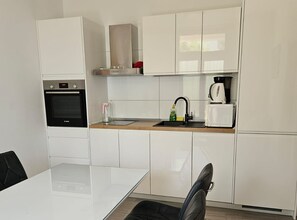 A modern kitchen with white cabinetry, a built-in oven, a coffee maker, and a sink. - Two Bedroom Apartment in ground floor (Trogir)