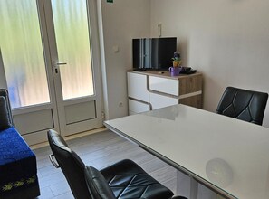A hotel room with a glass door, a flat-screen TV, a wooden desk, and a dining table with chairs. - Two Bedroom Apartment in ground floor (Trogir)