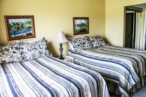 Una habitación con dos camas, cada una con ropa de cama estampada, una mesita de noche con lámpara y dos cuadros en la pared.