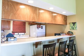 Una cocina con armarios de madera, un refrigerador blanco, un lavamanos y una zona de bar con sillas.