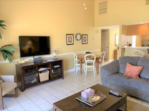A living room with a television, a sofa, a coffee table, and a dining area with chairs and a table. - Lake Views and Plenty of Room for All! (Palm Desert)