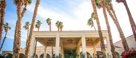 A building with a covered entrance, palm trees, and a clear sky.
