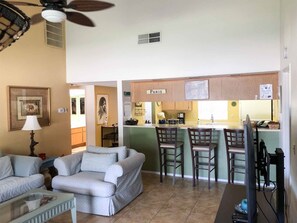 A living room with a sofa, a coffee table, and a TV. There is a kitchen area with a bar and chairs. - Enjoy the Outdoors on the 16th Fairway! (Palm Desert)