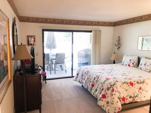 A bedroom with a bed, a desk, a chair, a lamp, and a sliding glass door leading to an outdoor area. - Enjoy the Outdoors on the 16th Fairway! (Palm Desert)