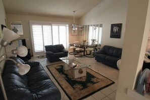A living room with a sofa, a coffee table, and a lamp. There is a dining area with a table and chairs. - Spacious and Comfy on the 15th Fairway! (Palm Desert)
