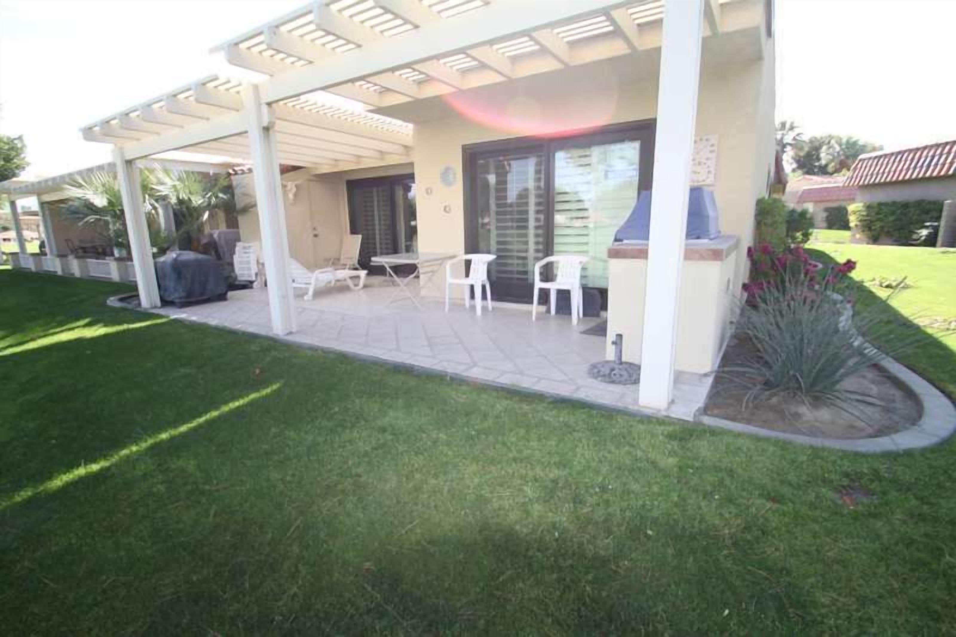 A covered patio area with outdoor seating, a barbecue grill, and a landscaped garden.