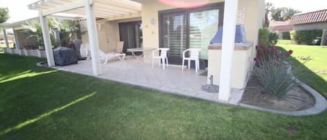 A covered patio area with outdoor seating, a barbecue grill, and a landscaped garden.