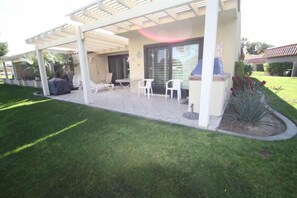 A covered patio area with outdoor seating, a barbecue grill, and a landscaped garden. - Spacious and Comfy on the 15th Fairway! (Palm Desert)