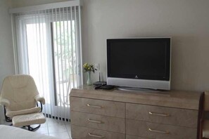 A room with a television on a cabinet, a chair, and a window with blinds. - Spacious and Comfy on the 15th Fairway! (Palm Desert)