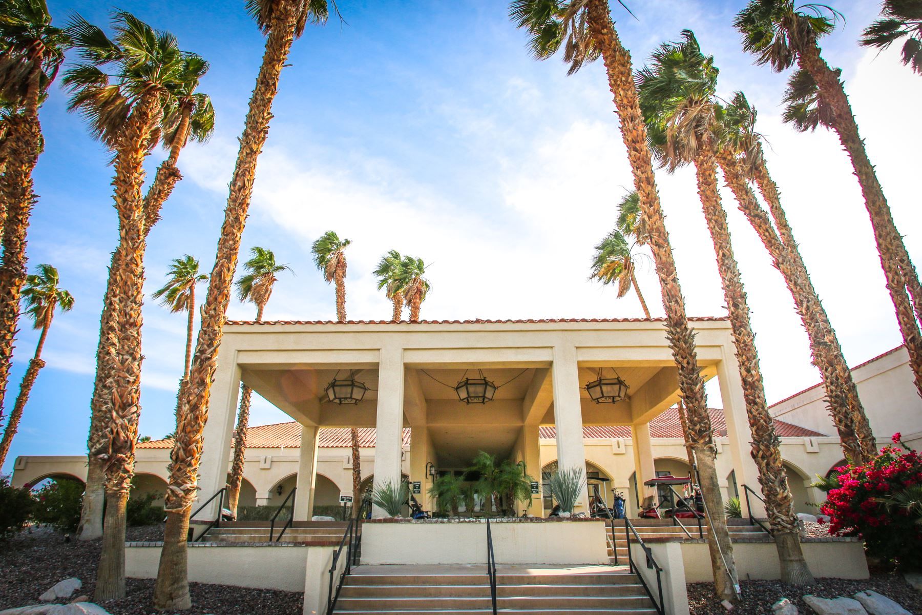 A building with a covered entrance, palm trees, and a clear sky.