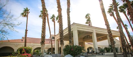 A building with a covered patio area, palm trees, and a clear sky.