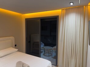 Habitación de hotel con cama, una silla y un ventanal que da a un balcón con mesa y sillas.