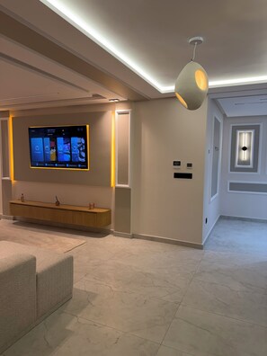 Ein modernes Interieur mit einem wandmontierten Flachbildfernseher, einem hölzernen Konsolentisch und einer deckenebnen Leuchte.