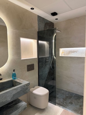 Un baño moderno con ducha de vidrio, lavamanos de mármol y estante empotrado.